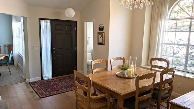 dining area with hardwood / wood-style flooring, vaulted ceiling, and an inviting chandelier