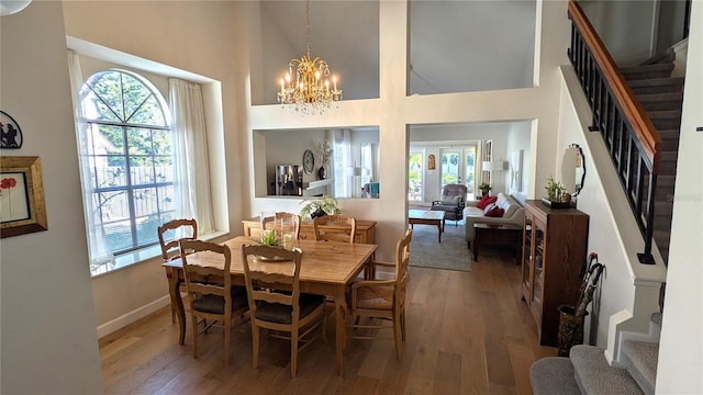 dining area with a healthy amount of sunlight, wood-type flooring, and a towering ceiling