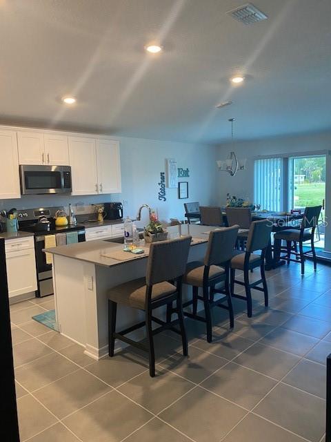 kitchen with white cabinets, tile patterned flooring, an island with sink, and appliances with stainless steel finishes