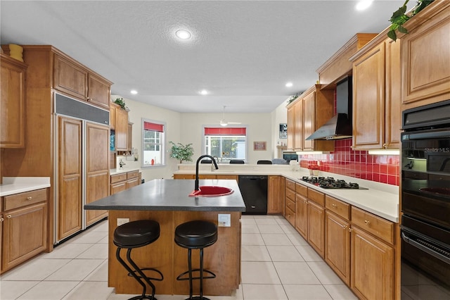 kitchen with wall chimney range hood, backsplash, a kitchen bar, a kitchen island with sink, and black appliances