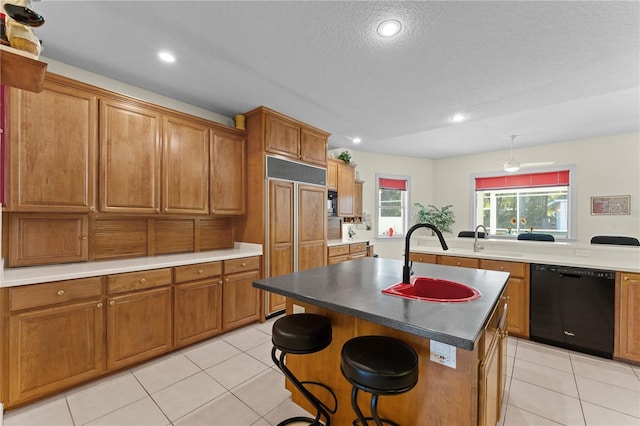 kitchen featuring sink, black dishwasher, paneled built in refrigerator, a kitchen bar, and a center island with sink