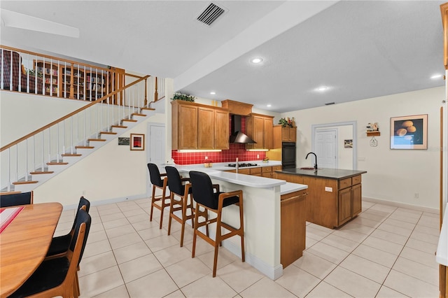 kitchen featuring backsplash, a kitchen island with sink, sink, wall chimney exhaust hood, and light tile patterned floors