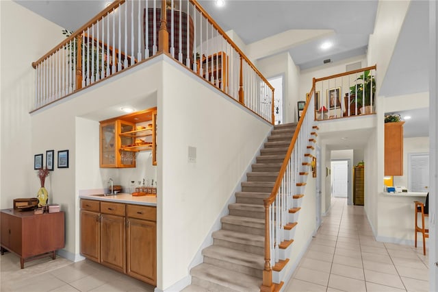 staircase with tile patterned floors, wet bar, and a towering ceiling