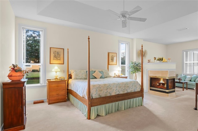 carpeted bedroom with a tray ceiling, ceiling fan, and a multi sided fireplace