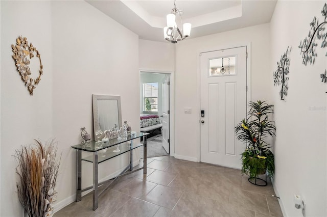 tiled foyer entrance featuring a tray ceiling and a chandelier