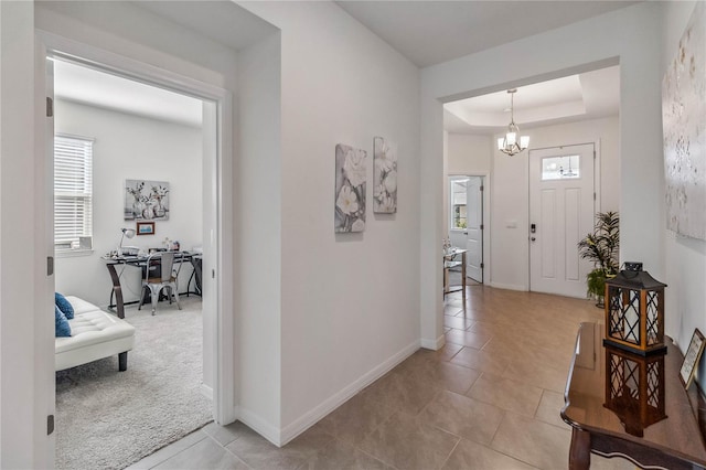 carpeted entryway featuring a tray ceiling and a notable chandelier