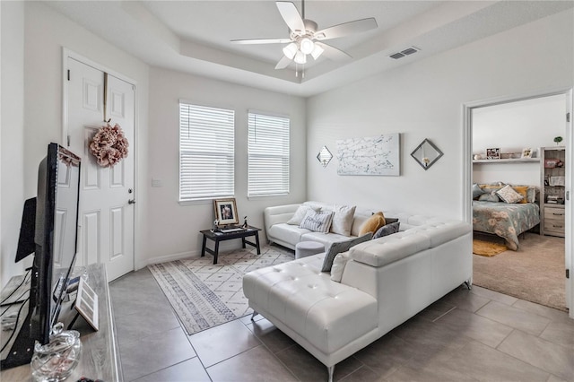 tiled living room featuring ceiling fan and a raised ceiling