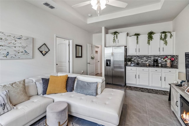 living room with a tray ceiling, tile patterned floors, and ceiling fan