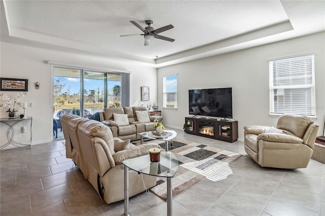 tiled living room featuring a textured ceiling, a tray ceiling, and ceiling fan