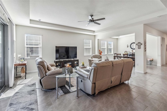 tiled living room with a tray ceiling, ceiling fan, a healthy amount of sunlight, and a textured ceiling