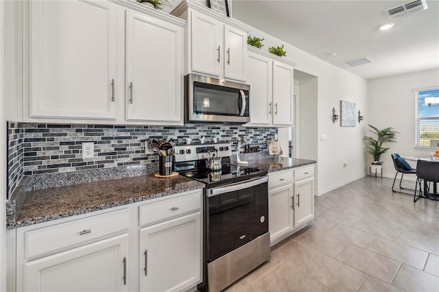 kitchen featuring dark stone counters, white cabinets, stainless steel appliances, and light tile patterned floors