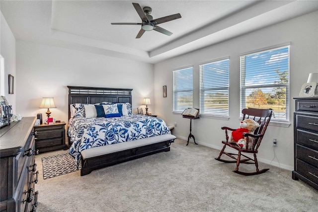 carpeted bedroom with multiple windows, a tray ceiling, and ceiling fan