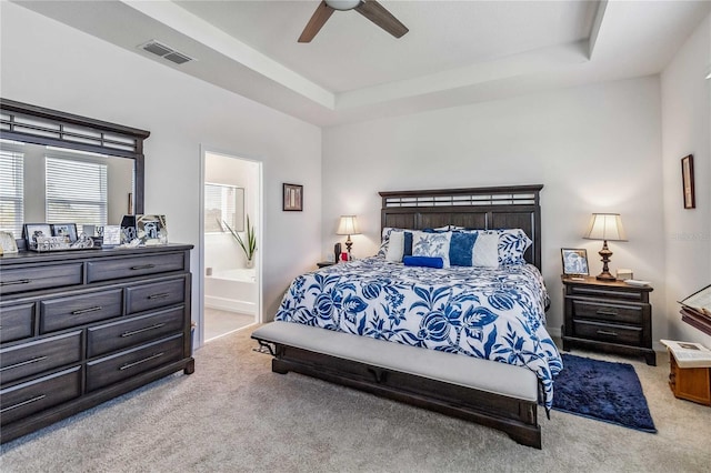 carpeted bedroom featuring a raised ceiling, ensuite bath, and ceiling fan