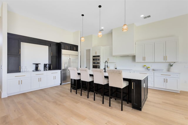 kitchen featuring stainless steel appliances, white cabinets, an island with sink, and hanging light fixtures