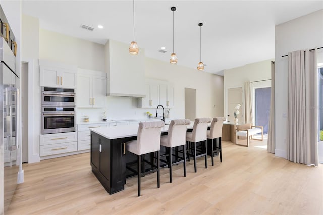 kitchen with stainless steel double oven, a kitchen island with sink, pendant lighting, and white cabinetry