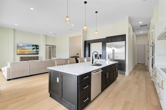 kitchen featuring a center island with sink, stainless steel appliances, sink, white cabinetry, and decorative light fixtures