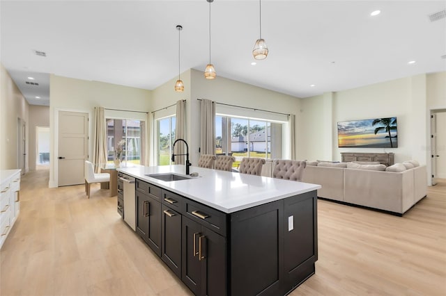 kitchen with sink, decorative light fixtures, light hardwood / wood-style flooring, and an island with sink