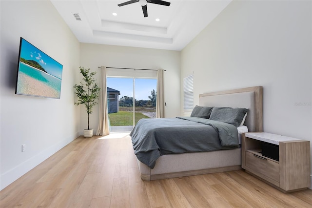 bedroom with ceiling fan, light hardwood / wood-style floors, access to outside, and a raised ceiling