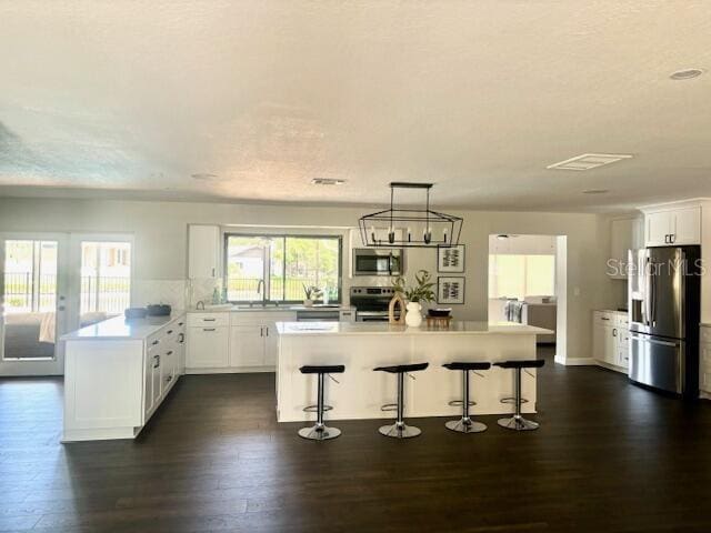 kitchen featuring pendant lighting, a center island with sink, white cabinets, appliances with stainless steel finishes, and a breakfast bar area