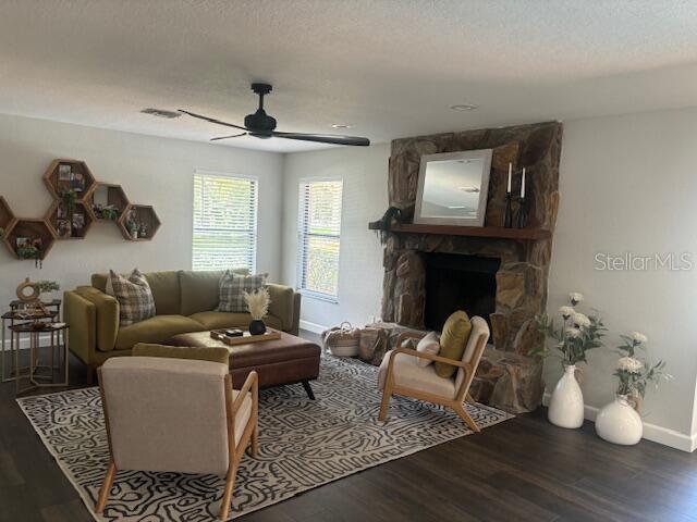 living room with hardwood / wood-style floors, a textured ceiling, a stone fireplace, and ceiling fan