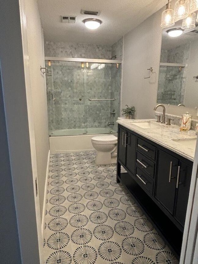 full bathroom featuring vanity, shower / bath combination with glass door, tile patterned floors, toilet, and a textured ceiling