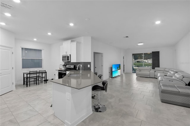 kitchen with sink, kitchen peninsula, a kitchen bar, white cabinetry, and stainless steel appliances