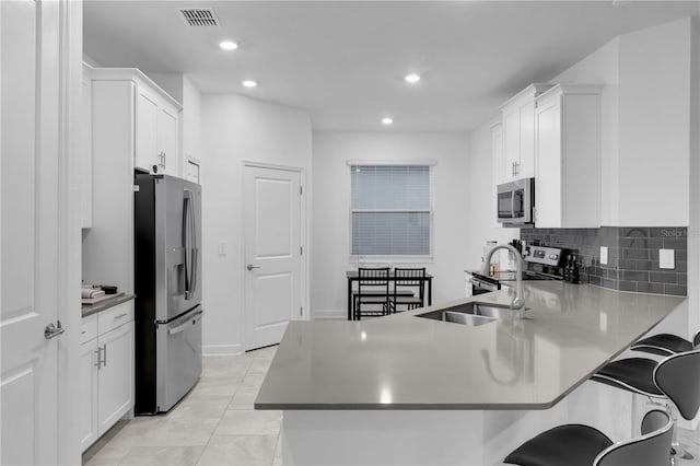 kitchen featuring white cabinets, a kitchen bar, kitchen peninsula, and stainless steel appliances