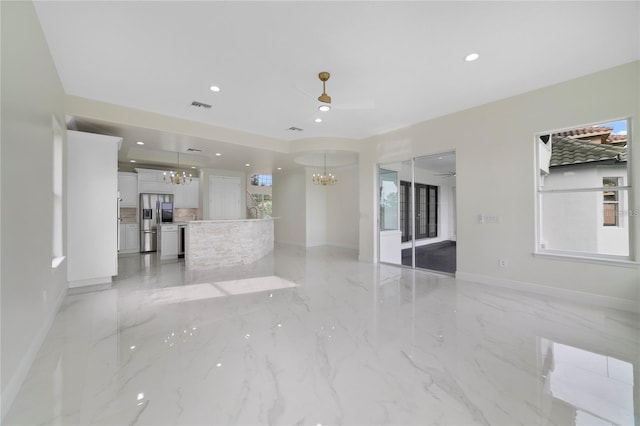 unfurnished living room with ceiling fan with notable chandelier