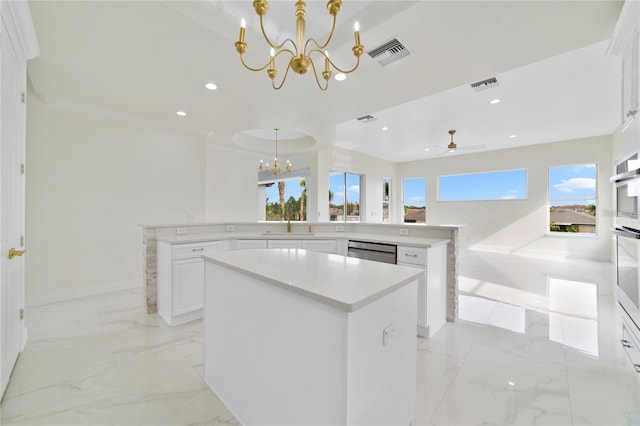 kitchen featuring ceiling fan with notable chandelier, hanging light fixtures, stainless steel dishwasher, a kitchen island, and white cabinetry