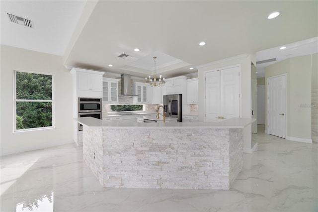 kitchen featuring white cabinetry, a spacious island, wall chimney range hood, and decorative light fixtures