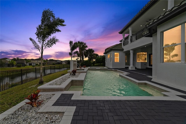 pool at dusk with a water view and a patio