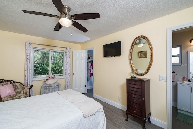 bedroom featuring a walk in closet, a textured ceiling, ceiling fan, dark hardwood / wood-style floors, and a closet