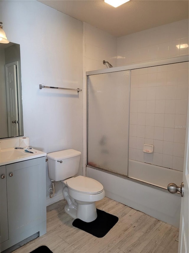 full bathroom featuring hardwood / wood-style flooring, toilet, combined bath / shower with glass door, and vanity