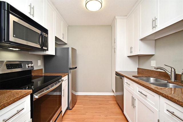 kitchen featuring dark stone counters, white cabinets, sink, appliances with stainless steel finishes, and light hardwood / wood-style floors