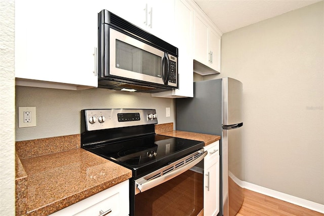 kitchen featuring dark stone counters, white cabinets, light hardwood / wood-style floors, and appliances with stainless steel finishes