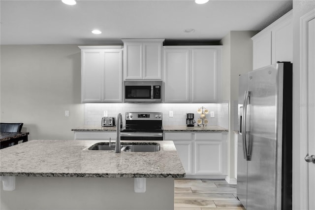 kitchen with sink, an island with sink, light hardwood / wood-style floors, white cabinets, and appliances with stainless steel finishes