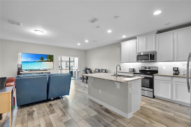 kitchen featuring white cabinets, sink, stainless steel appliances, and an island with sink