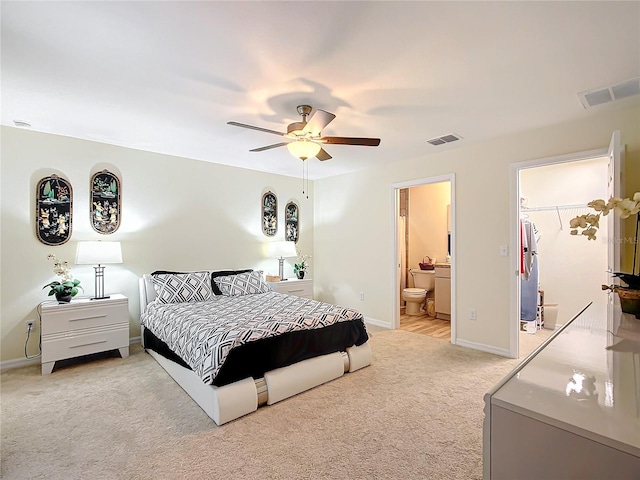 bedroom featuring a closet, ensuite bath, light colored carpet, ceiling fan, and a walk in closet