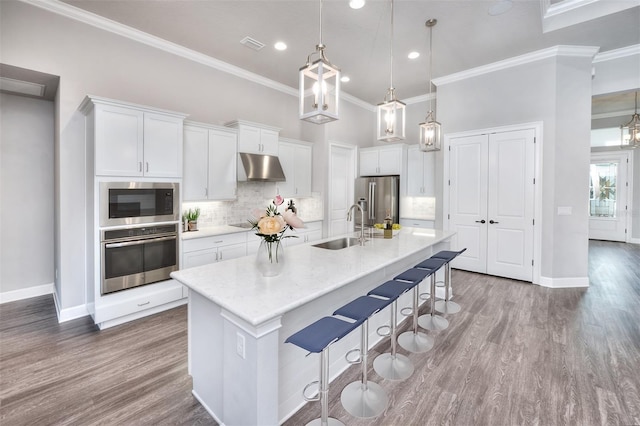 kitchen with sink, stainless steel appliances, an island with sink, decorative light fixtures, and white cabinets