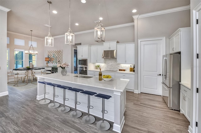 kitchen with white cabinetry, stainless steel refrigerator, hanging light fixtures, and sink