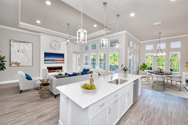 kitchen featuring a large fireplace, sink, hanging light fixtures, a kitchen island with sink, and white cabinets