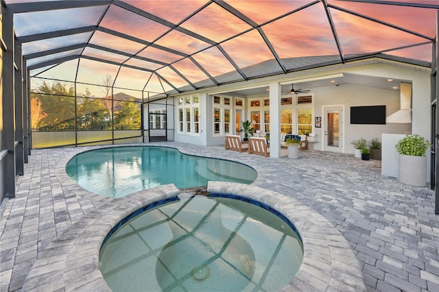 pool at dusk featuring an in ground hot tub, french doors, ceiling fan, glass enclosure, and a patio