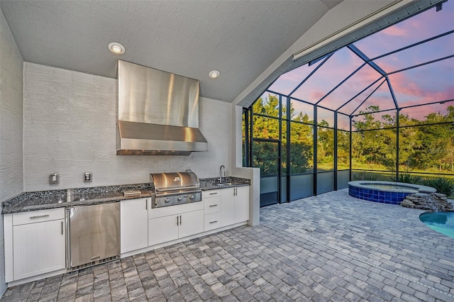 patio terrace at dusk featuring glass enclosure, sink, a grill, area for grilling, and an in ground hot tub