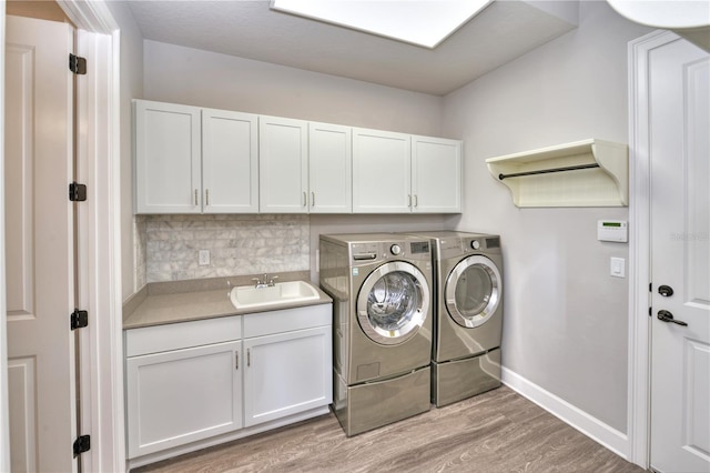 clothes washing area featuring separate washer and dryer, sink, cabinets, and light wood-type flooring