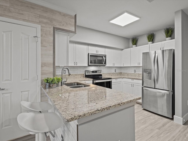 kitchen with white cabinets, stainless steel appliances, sink, kitchen peninsula, and a breakfast bar