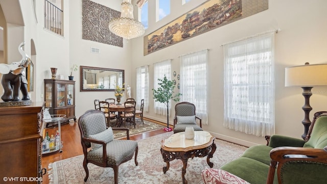 living area with an inviting chandelier, a towering ceiling, wood-type flooring, and a wealth of natural light