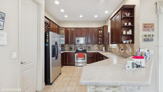 kitchen featuring light tile patterned floors, appliances with stainless steel finishes, dark brown cabinetry, decorative backsplash, and kitchen peninsula