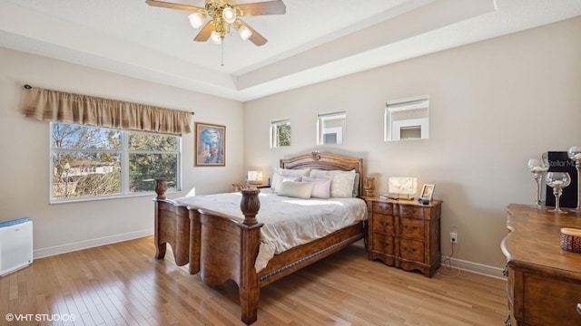 bedroom with a tray ceiling, ceiling fan, and light wood-type flooring