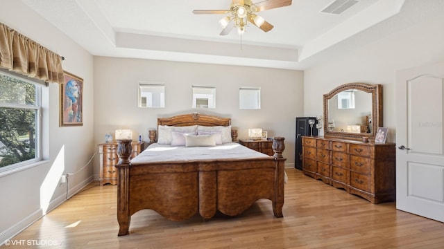 bedroom with ceiling fan, light hardwood / wood-style floors, and a tray ceiling