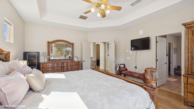 bedroom with light hardwood / wood-style flooring, a raised ceiling, and ceiling fan